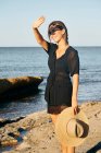Молодая привлекательная женщина покрывает лицо от солнца на пляже и держит шляпу — стоковое фото