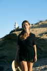 Junge nachdenkliche Frau genießt Sonne und schaut am Strand weg mit Leuchtturm im Hintergrund — Stockfoto