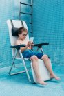 Чоловік використовує смартфон, відпочиваючи на стільці у порожньому басейні, прикрашеному синьою плиткою — стокове фото