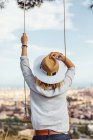 View from behind of a girl with a hat looking at the city next to a swing — Stock Photo
