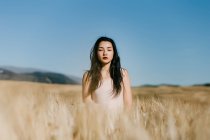 Mulher asiática bonita olhando para a câmera enquanto está de pé no fundo borrado do prado no dia ventoso na natureza — Fotografia de Stock