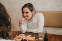 Attraente giovane donna che pranza con un amico e degustazione spuntino appetitoso a tavola — Foto stock