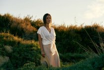 Jovem mulher atraente em roupas brancas olhando para a câmera na natureza ao pôr do sol — Fotografia de Stock