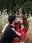 Uomo che abbraccia sorridente moglie incinta seduta in grembo sullo sfondo del pittoresco parco verde — Foto stock