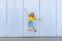 Young cheerful woman jumping in air on blue background — Stock Photo