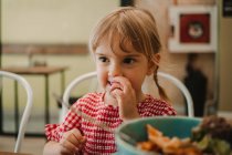 Appetizing comida variada fragrante em tigela azul e menina adorável comer à mesa — Fotografia de Stock
