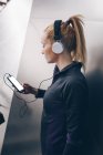 Молодая белокурая белая женщина в спортивной одежде слушает музыку с наушниками, подключенными к ее смартфону — стоковое фото