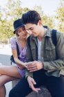 Young handsome man with girlfriend using phone while sitting in beautiful garden — Stock Photo