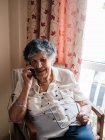 Щаслива старша жінка посміхається і розмовляє по мобільному телефону, дивлячись вдома — стокове фото