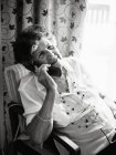Heureuse femme âgée souriante et parlant sur un téléphone portable tout en regardant loin à la maison — Photo de stock