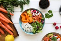 Du dessus bol de riz bouilli délicieux avec divers légumes frais placés sur une table blanche près de la sauce soja — Photo de stock