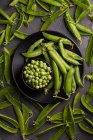 Peeled fresh peas and pea pods on dark wooden table — Stock Photo