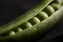 Peeled fresh peas in pod on dark background — Stock Photo