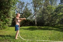 Little laughing kid in shorts and with bare feet splashing water from garden hose — Stock Photo