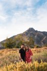 Мужчина и улыбающаяся беременная жена смотрят в камеру на фоне природы и гор — стоковое фото