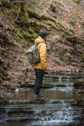 Vue latérale d'un homme anonyme avec sac à dos debout sur des marches naturelles avec de l'eau vive et en terrain montagneux — Photo de stock