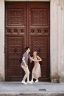 Joven pareja alegre y juguetona en ropa casual divirtiéndose durante citas al aire libre frente a la hermosa puerta vieja - foto de stock