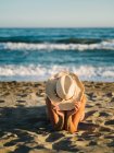 Tanned unrecognizable woman in hat lying sunbathing on sandy seaside in sunny day — Stock Photo