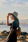 Young female tourist wearing a straw hat and backpack standing near beach — Stock Photo