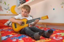 Jeune garçon blonde jouant de la guitare jouet — Photo de stock
