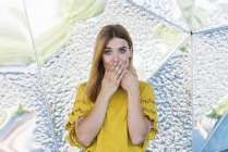 Giovane donna giocosa che copre la bocca con le mani su sfondo metallico — Foto stock
