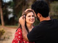 Mann lächelt Frau in verschwommener Natur an und setzt Blume ins Haar — Stockfoto