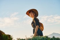 Туристка в соломенной шляпе и рюкзаке, гуляющая на природе и смотрящая в камеру — стоковое фото