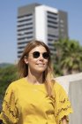 Веселая молодая женщина в солнечных очках улыбается и смотрит вдаль в городе — стоковое фото