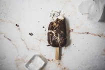 Se estrelló vainilla y helado de chocolate paleta en la superficie de mármol con cubitos de hielo - foto de stock