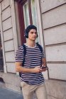 Привабливий молодий чоловік в повсякденному одязі слухає музику під час ходьби на вулиці в денний час — стокове фото