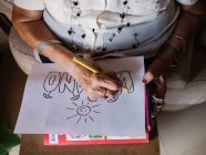 Imagem cortada de mulher sênior em camisa branca e óculos desenhando em papel com lápis, sentado em poltrona em casa — Fotografia de Stock