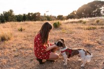 Junge Frau mit langen Haaren spielt und gibt Zuneigung zu niedlichen Hund — Stockfoto
