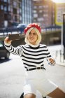 Junge lächelnde hübsche Frau mit französischer roter Mütze, gestreifter Bluse und weißen Shorts, die ein Foto auf städtischem Hintergrund macht — Stockfoto