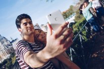 Joven hombre guapo tomando selfie con novia en hermoso jardín - foto de stock