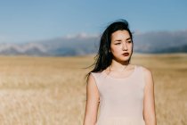 Mulher asiática bonita olhando para longe, enquanto de pé no fundo borrado do prado no dia ventoso na natureza — Fotografia de Stock