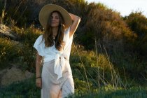Молода приваблива жінка в білому одязі дивиться на камеру в природі на заході сонця — стокове фото