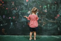 Vista posteriore del bambino adorabile irriconoscibile che disegna a scuola durante la lezione in una lavagna verde — Foto stock