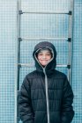 Smiling male kid in warm jacket standing on background of pool wall and looking at camera — Stock Photo