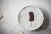 Шоколадное мороженое эскимо на тарелке с кубиками льда на мраморной поверхности — стоковое фото