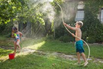 Little children in swimwear running around and splashing water from garden hose at each other — Stock Photo