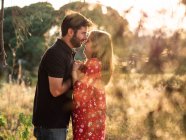 Uomo che abbraccia sorridente moglie incinta sullo sfondo del pittoresco parco verde nella giornata di sole — Foto stock