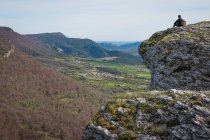 Vue latérale d'un homme méconnaissable portant un sac à dos assis sur une montagne et admirant une vue pittoresque des champs et des collines — Photo de stock