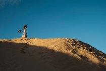 Женщина в белом платье, стоящая вдали на солнце освещенный песчаный холм в Тарифе, Испания с голубым небом и белым облаком — стоковое фото