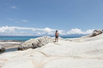 Homme mûr bronzé debout sur le rivage rocheux blanc avec ciel bleu et nuages, Halkidiki, Grèce — Photo de stock
