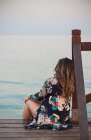 Young brunette woman resting on dock near water surface and looking at coastline — Stock Photo