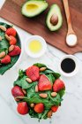 Bowls with strawberry, almond and greenery salad on table with avocado and spoon of sauce on cutting board — Stock Photo