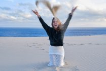 Allegro giocoso donna gettando mucchio di sabbia alla macchina fotografica mentre seduto sulla costa vuota a Tarifa, Spagna — Foto stock