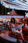 Fröhlich schöne Frau genießt Fahrt auf Karussell auf Jahrmarkt während Sommerabend auf verschwommenem Hintergrund — Stockfoto