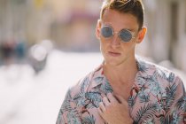 Handsome male in Hawaiian shirt standing on street with sunglasses, looking away — Stock Photo