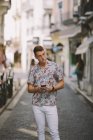 Красивый мужчина в гавайской рубашке стоит на улице, пользуется мобильным телефоном и отворачивается. — стоковое фото